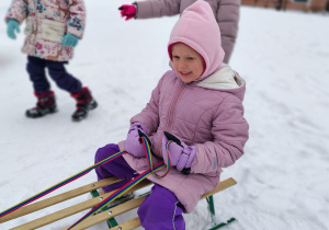 Dziewczynka siedzi na sankach.