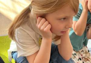 Dziewczynka trzyma się za uszy.