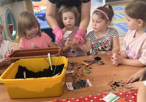 Nauczycielka pomaga dzieciom sadzić kwiatki.