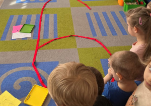 Dzieci przygladają się dużej cyfrez ułożonej na dywanie.