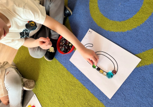 Dziecko ozdabia cyfrę kamyczkami.