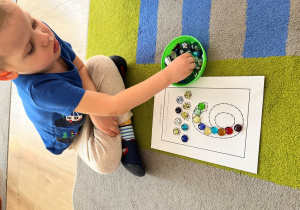 Chłopiec ozdabia kamyczkami cyfrę.