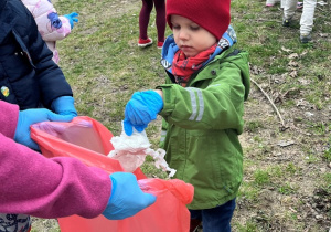 Chłopiec wkłada śmieć do worka.
