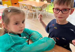 Dziewczynka w roli lekarza bada chłopca.