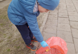 Chłopiec wkłada śmieć do worka.