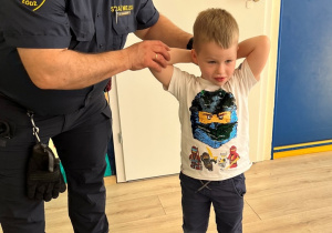 Pracownik Straży Miejskiej pokazuje na chłopcu ułożenie rąk podczas ataku psa.