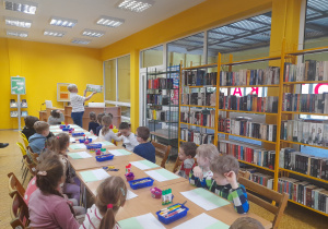 Dzieci słuchają bajki czytanej przez Panią pracującą w bibliotece.