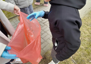 Dziecko wrzuca zebrane śmieci do worka.