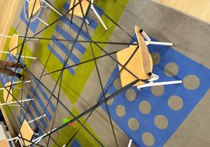 Na krzesłach usrtawionych na dywanie rozciągnięta taśma.