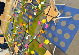 Pajęczyna wykonana z taśmy i krzeseła z zapiętymi kwiatkami.