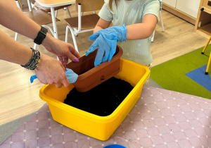 Dziewczynka wsypuje ziemię do doniczki.