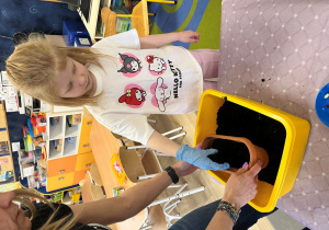 Dziewczynka dosypuje ziemię do skrzynki.