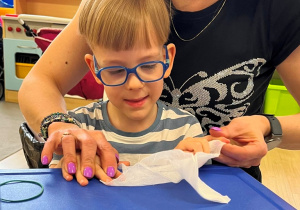 Nauczycielka pomaga chłopcu rozłożyć gazę.