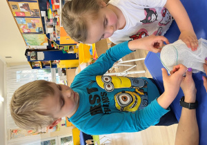 Dzieci zakładaja gumkę na słoik z gazą.