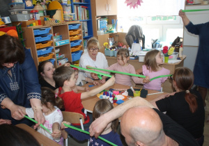 Dzieci z rodzicami tworzą kwiaty z krepiny.