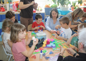 Dzieci z rodzicami tworzą kwiaty z krepiny.