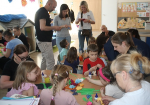 Dzieci z rodzicami tworzą kwiaty z krepiny.