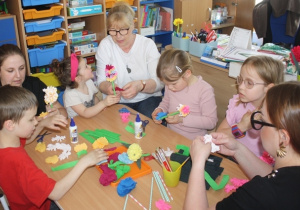 Dzieci z rodzicami tworzą kwiaty z krepiny.