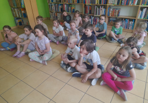 Dzieci siedzą w bibliotece na poduszkach.