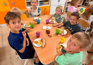 Dzieci jedzą pizzę.
