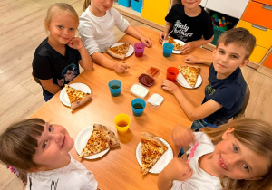 Dzieci jedzą pizzę.