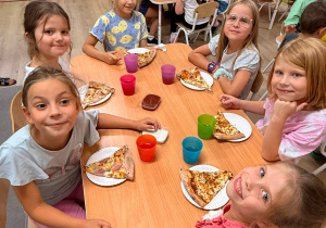 Dzieci jedzą pizzę.
