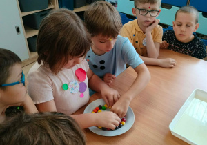 Dzieci wykładają skitllesy na talerz.