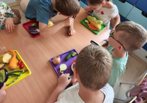 Dzieci uważnie przyglądają się warzywom przez szkło powiększające.