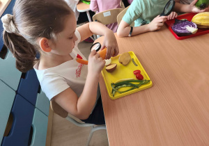 Dziewczynka ogląda marchewkę przez lupę.