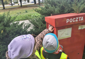 Dzieci wrzucają kartkę do skrzynki pocztowej.