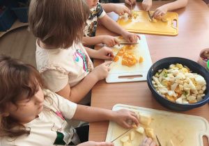 Dzieci samodzielnie kroją nożem owoce do sałatki.