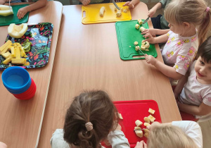 Dzieci samodzielnie kroją nożem owoce do sałatki.