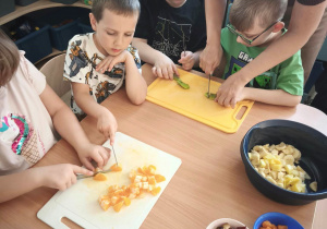 Dzieci z pomocą nauczyciela kroją owoce.