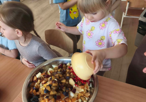 Dziewczynka wrzuca pokrojone owoce do miski.