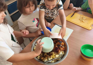Dzieci dodają skrojone owoce do miski.