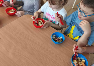 Dzieci ze smakiem jedzą samodzielnie skomponowaną sałatkę owocową.