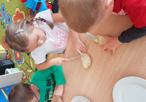 Dzieci smarują kanapki masłem.