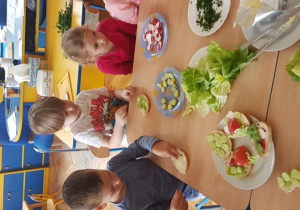 Dzieci dekorują kanapki warzywami.