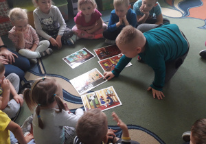 dzieci siedzą na dywanie, jeden z chłopców wskazuje palcem na odpowiedni obrazek