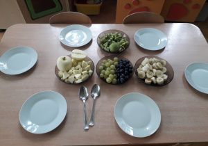 Na stole stoją pokrojone owoce w miskach