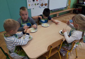 Dzieci siedzą przy stole i robią szaszłyki