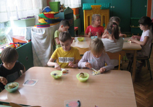 Dzieci siedzą i kroją owoce.