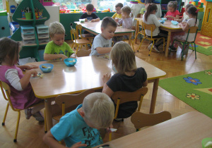 Dzieci siedzą i kroją owoce.
