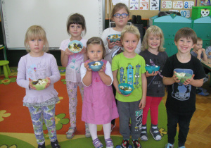 Dzieci stoją i prezentują swoje sałatki owocowe.