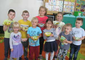 Dzieci stoją i prezentują swoje sałątki owocowe.