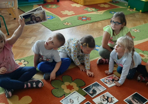 Dzieci siedzą na dywanie. Dziewczynka pokazuje obrazek.