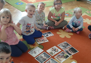 Dzieci siedzą na dywanie. Oglądają obrazki z emocjami.
