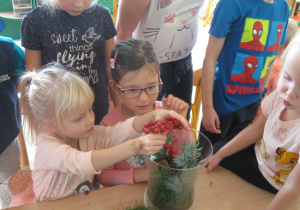 Dzieci wkładają galązki do wazonu.