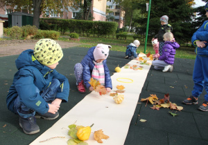 Dzieci układają kolorowe liście na pasie białego papieru.