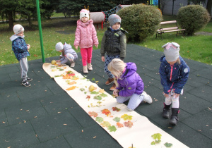 Dzieci układają kolorowe liście na pasie białego papieru.